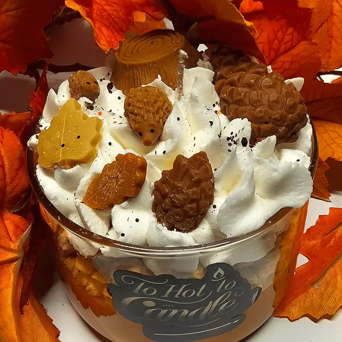 Herfstgeurkaars in glazen pot met decoratieve topping van slagroom-look, dennenappels, eikels en blaadjes