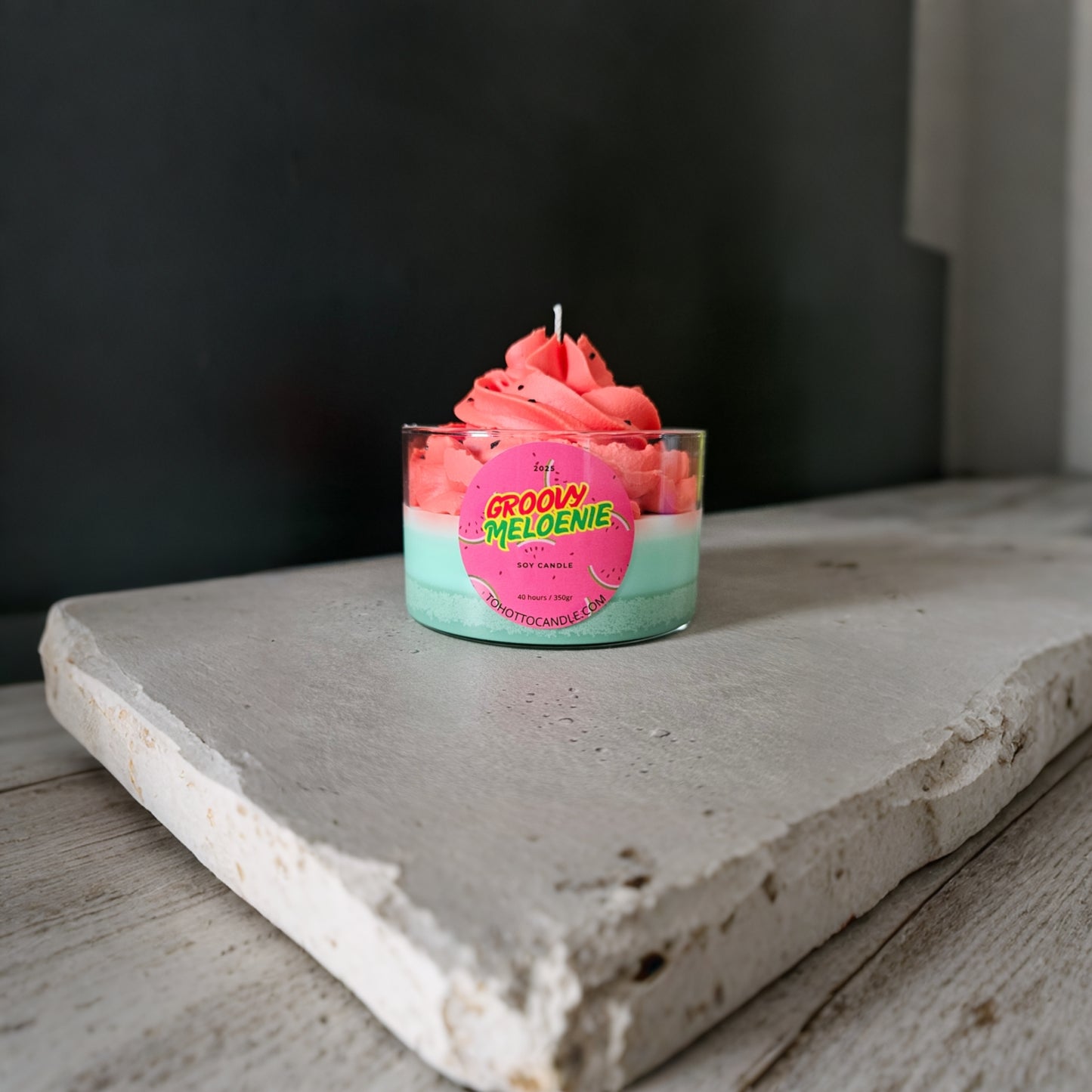 Groovy Meloenie geurkaars met roze topping op een witte rustieke betontafel.