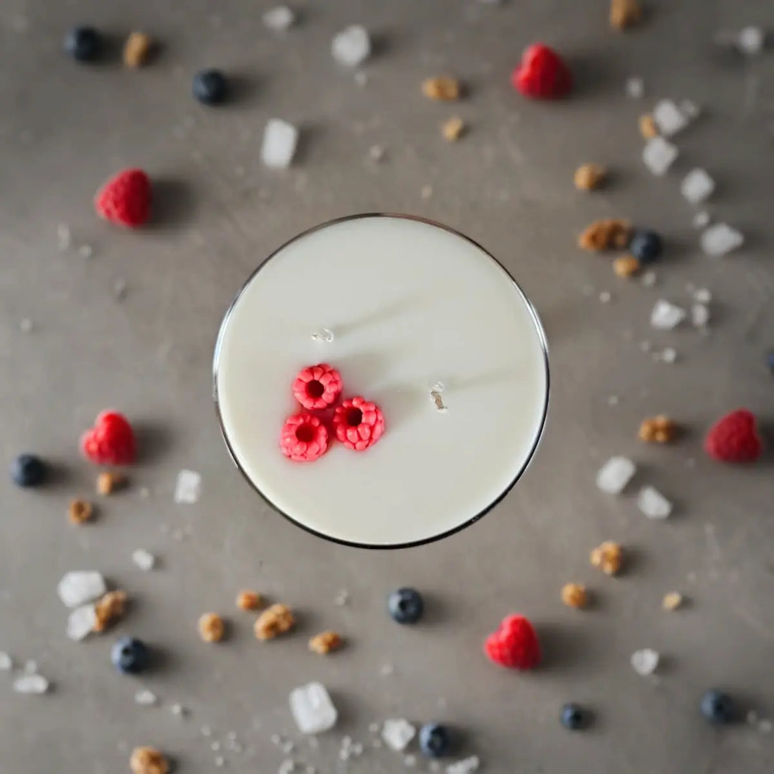 Cocktail kaars bovenaanzicht omringd door frambozen en fruit op een tafel