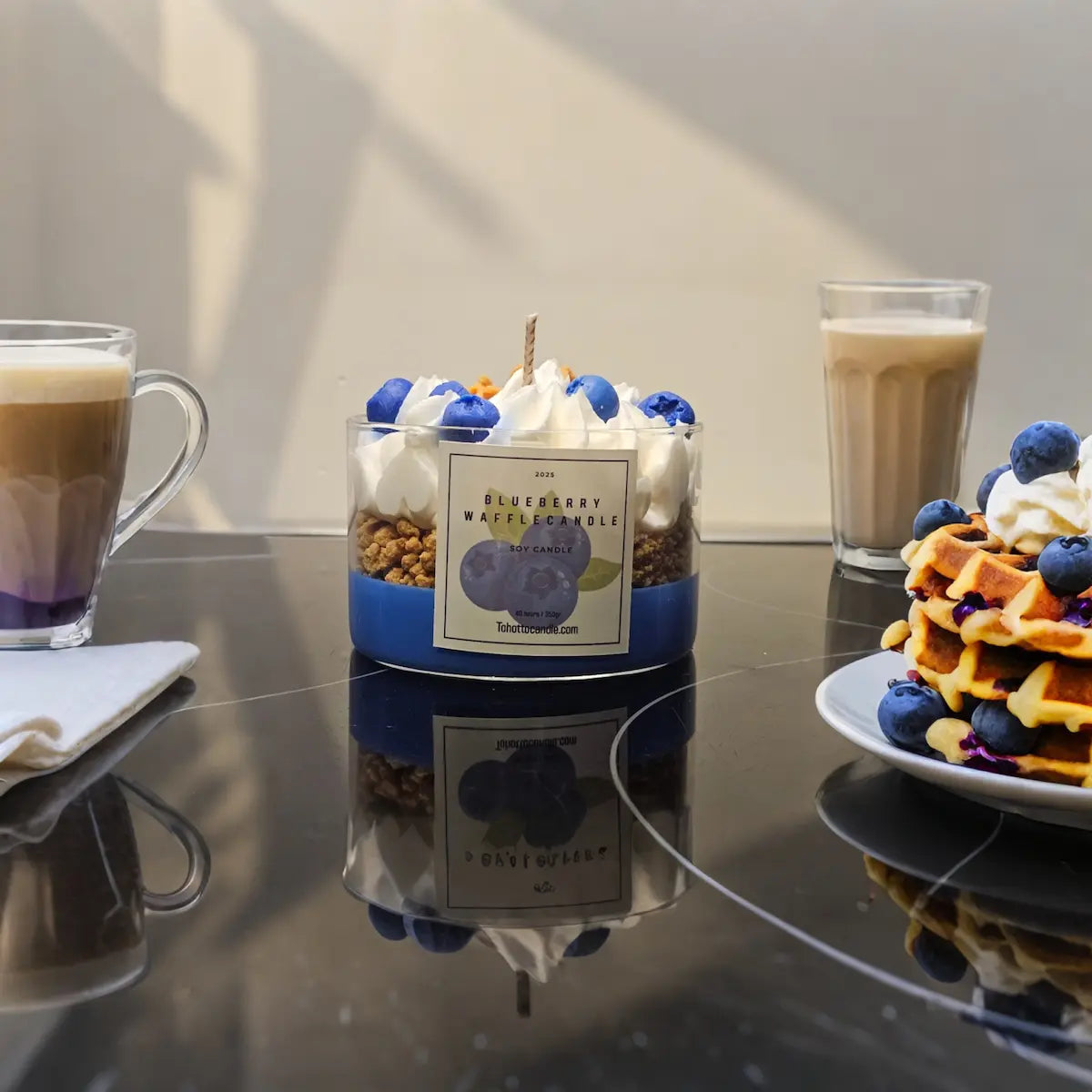 Handgemaakte blauwe sojakaars met slagroomlook tussen koffie en wafels op ontbijttafel.
