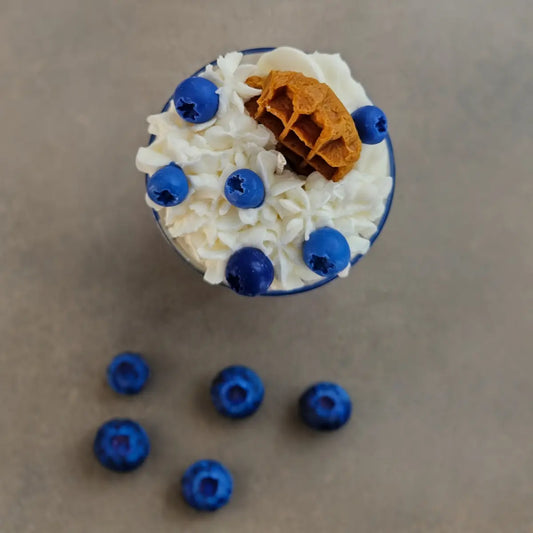 Decoratieve geurkaars met blauwe bessen op tafel.