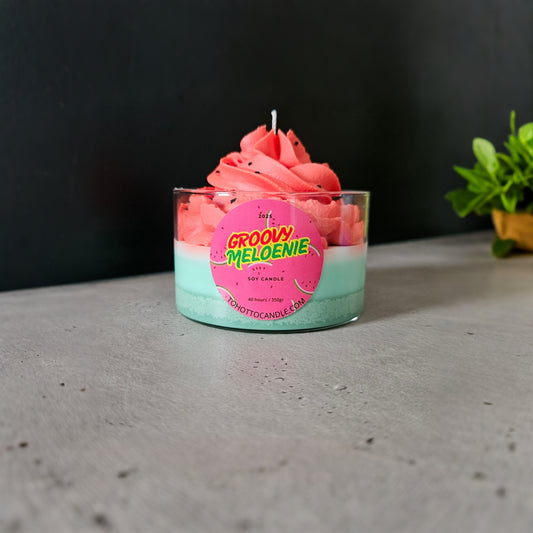 Groovy Meloenie sojakaars met roze topping op grijze tafel en groene plant op achtergrond.