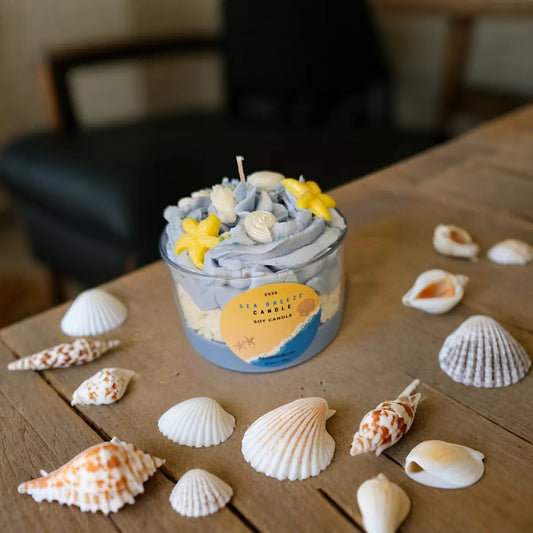 Geurkaars Sea Breeze met blauwe sojawas, versierd met schelpen en zeesterren, op houten tafel met echte schelpen eromheen.